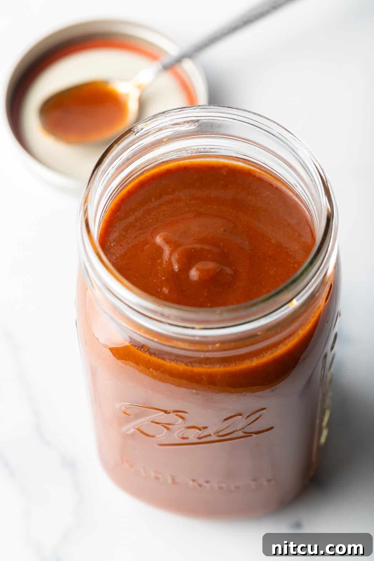 Top down view of red sauce in a large glass jar.