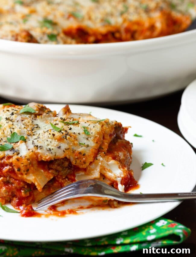 A delicious slice of Italian sausage lasagna on a plate with a bite taken out, showcasing its rich, layered interior.