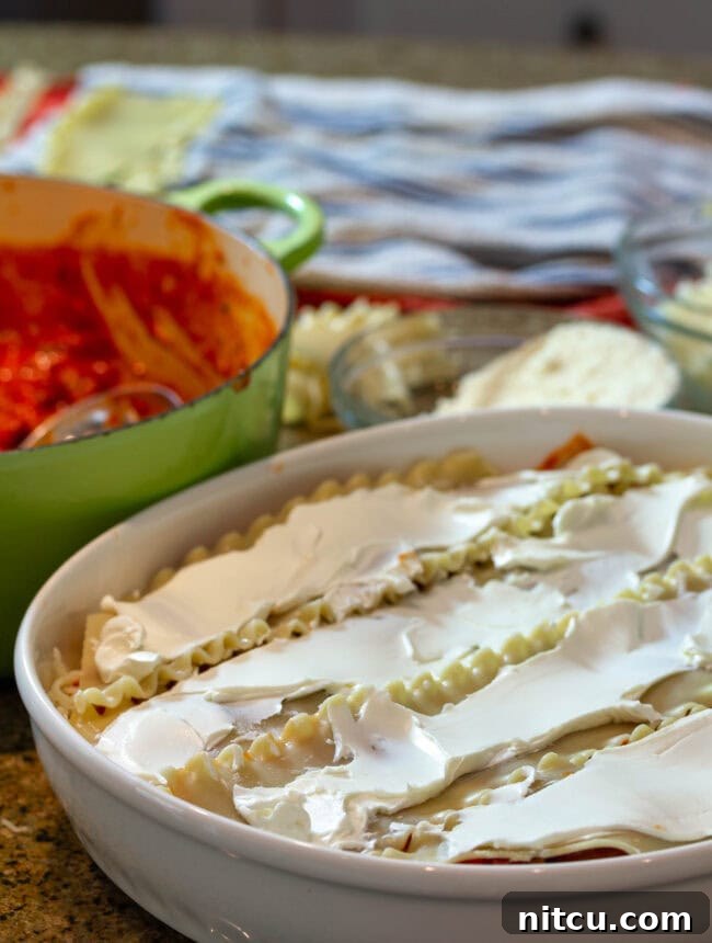 Chef's hands expertly layering pasta and cheese in a baking dish, forming the foundation of a delicious cream cheese lasagna.