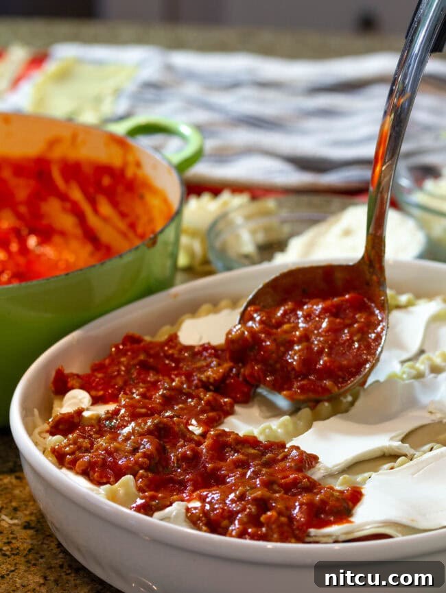 Adding a generous scoop of flavorful meat sauce to the layered cream cheese lasagna, building depth and richness.