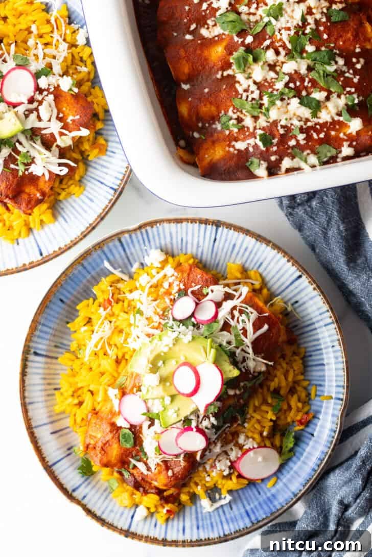 Large plate with 2 authentic enchiladas covered in red sauce, on a pile of fluffy yellow rice and topped with fresh cabbage slaw, sliced radishes, and avocado.