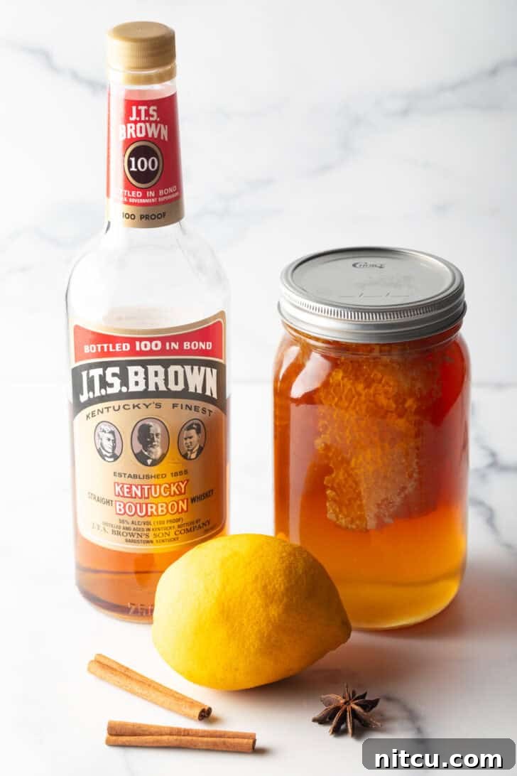 Recipe ingredients together: large mason jar of honey, whole lemon, and bottle of bourbon.