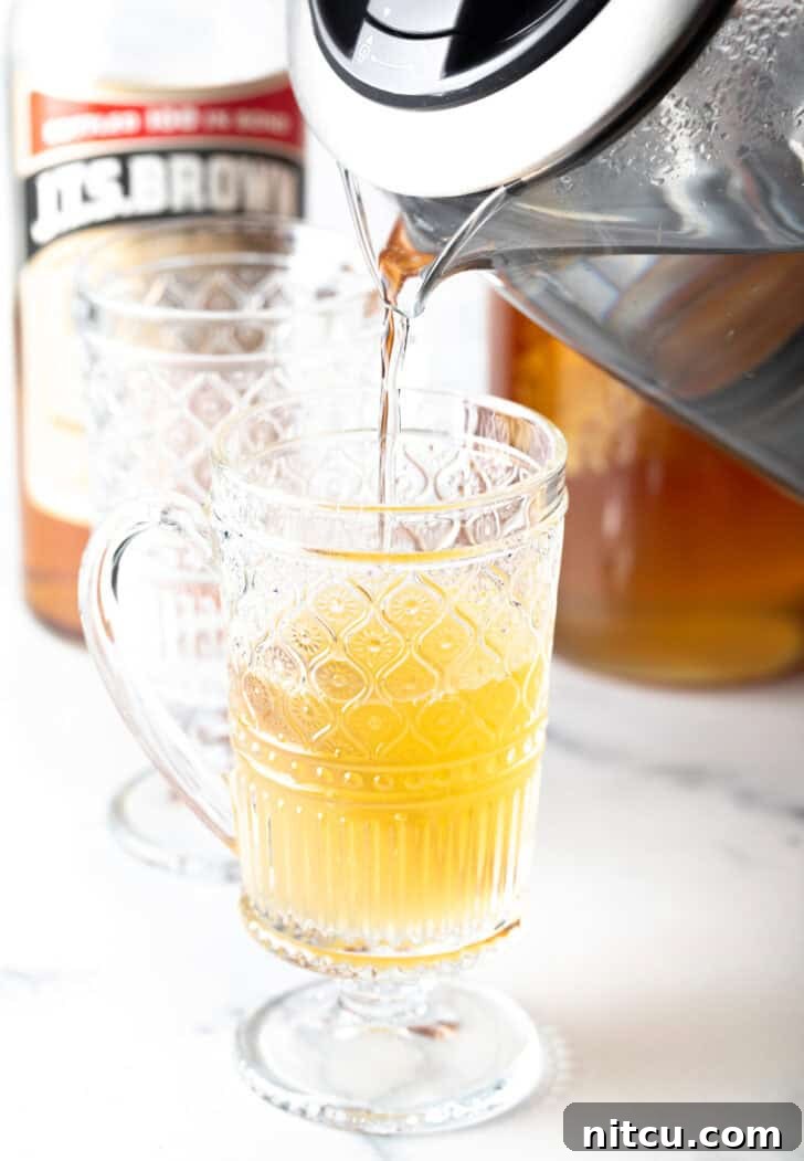 Pouring tea from a metal kettle into a clear glass mug.