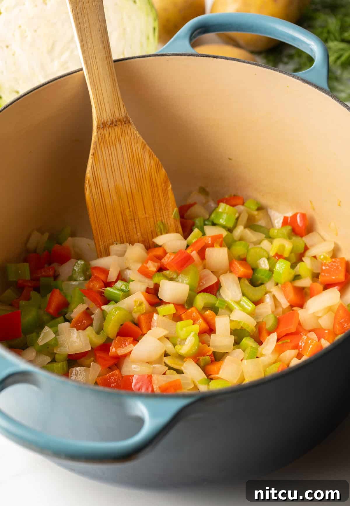Cooking diced onion, carrots, bell pepper and celery in a large blue cooking pot.