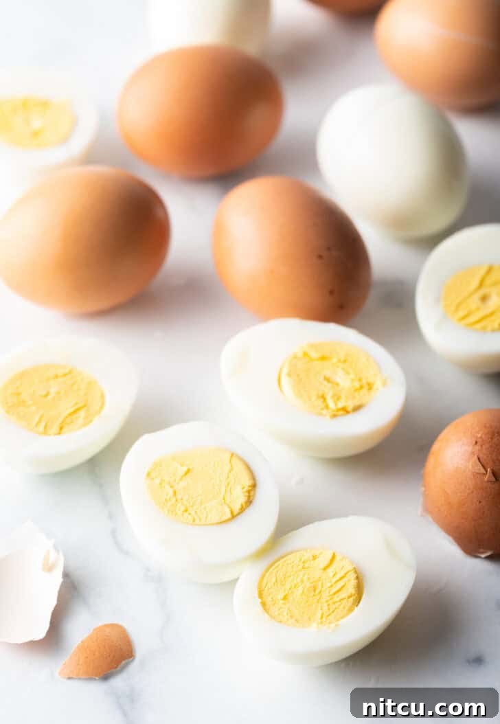 A dozen hard boiled eggs on a white marble backdrop. There are five egg halves, four brown eggs in the shell, and one white peeled egg.
