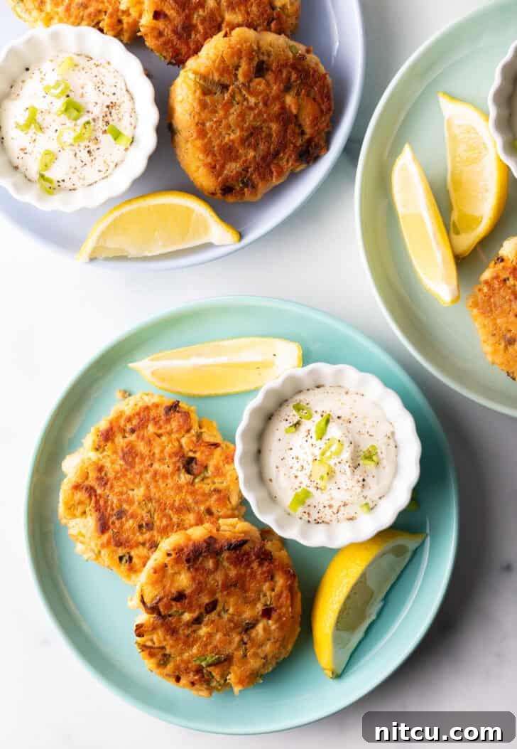 Two perfectly cooked salmon patties on a rustic green plate, garnished with a side of creamy tartar sauce in a white ramekin and fresh lemon wedges, ready to be served.