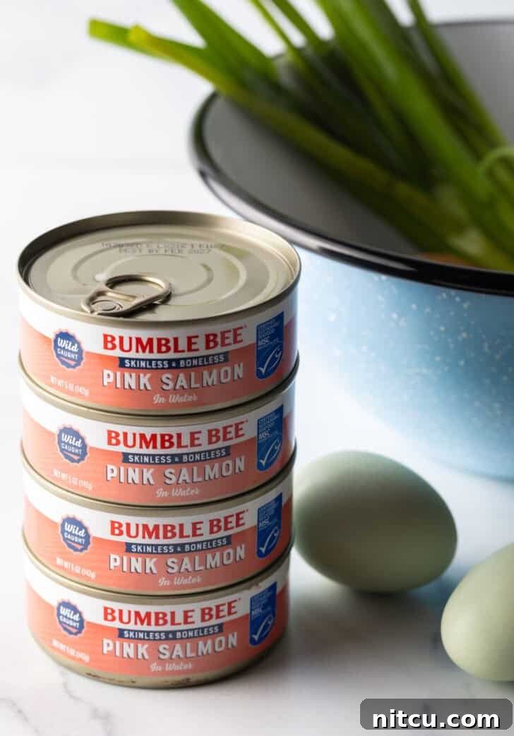 Four cans of pink canned salmon are neatly stacked, with a single white egg resting beside them, highlighting key ingredients for the recipe.