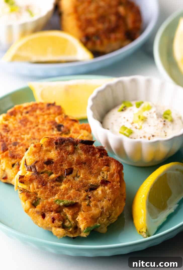 A vibrant green plate holds two salmon patties, accompanied by a small white ramekin of tartar sauce and two bright yellow lemon wedges, creating an appetizing presentation.