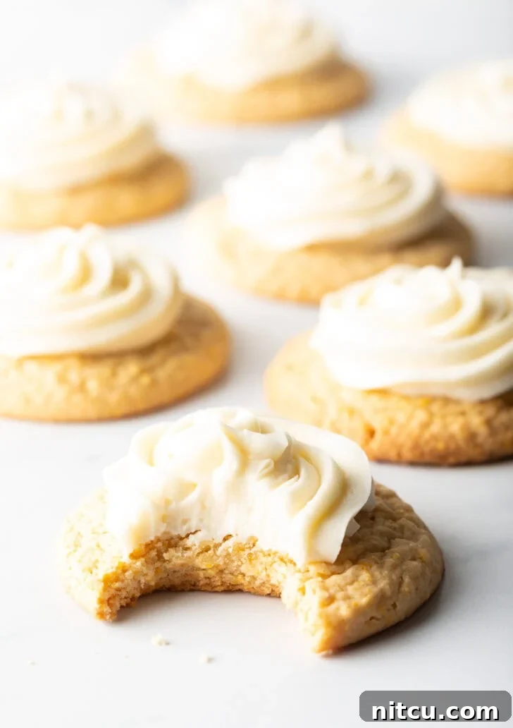 Several honey butter cornbread cookies on a white background, each topped with piped frosting. The cookie closest to camera has a bite taken out.
