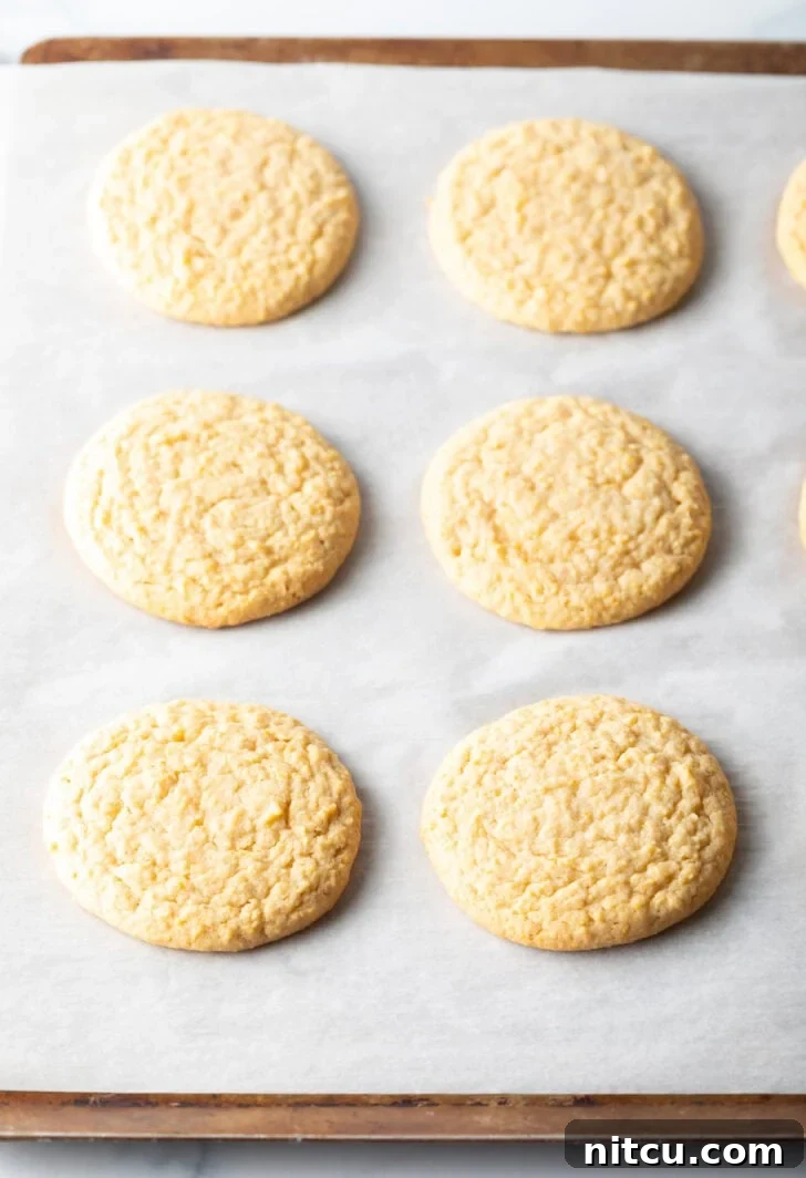 6 flat baked cornbread cookies on a baking sheet.