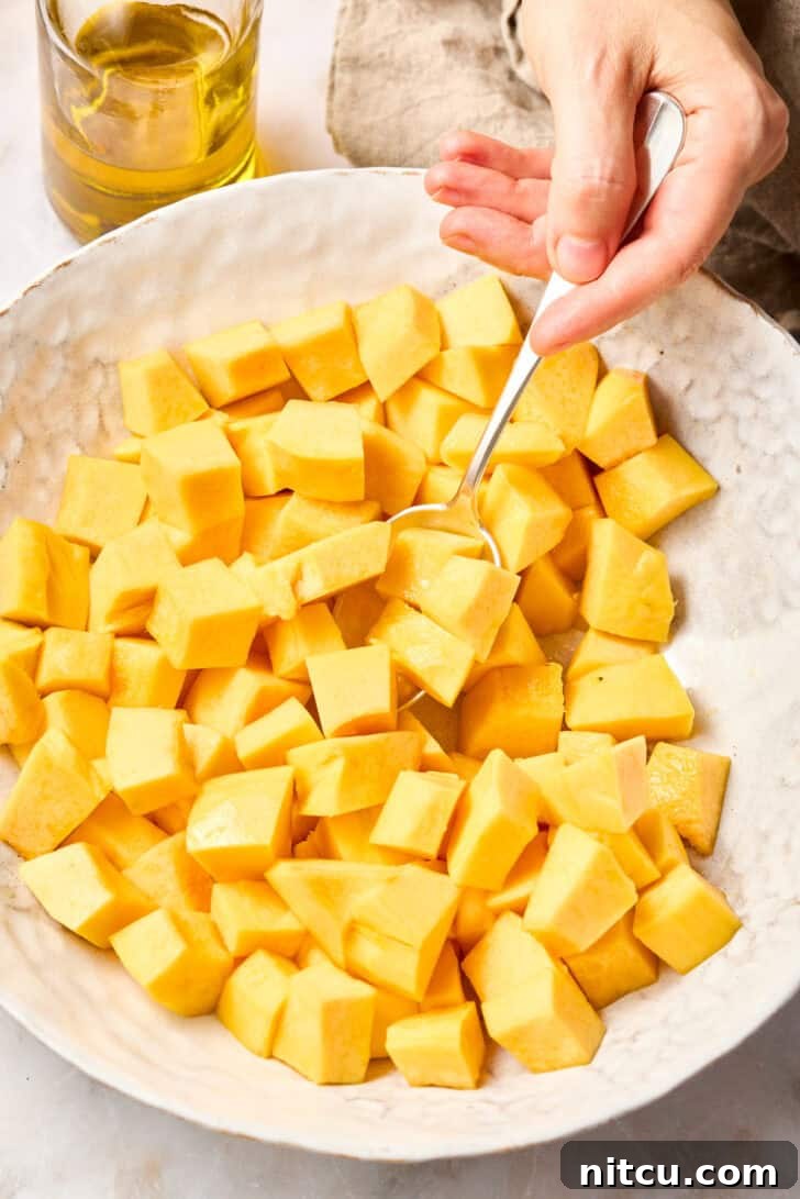 Chopped butternut squash in a bowl, drizzled with oil, ready for roasting.