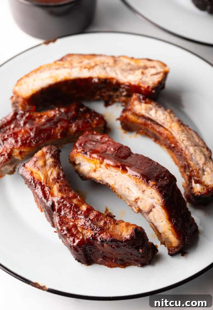 5 air fried baby back ribs on a white plate, garnished with fresh herbs.