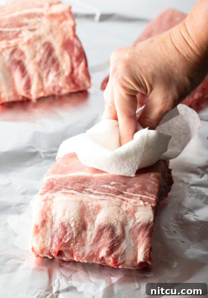 Hand using a paper towel to pat dry a small rack of baby back ribs.