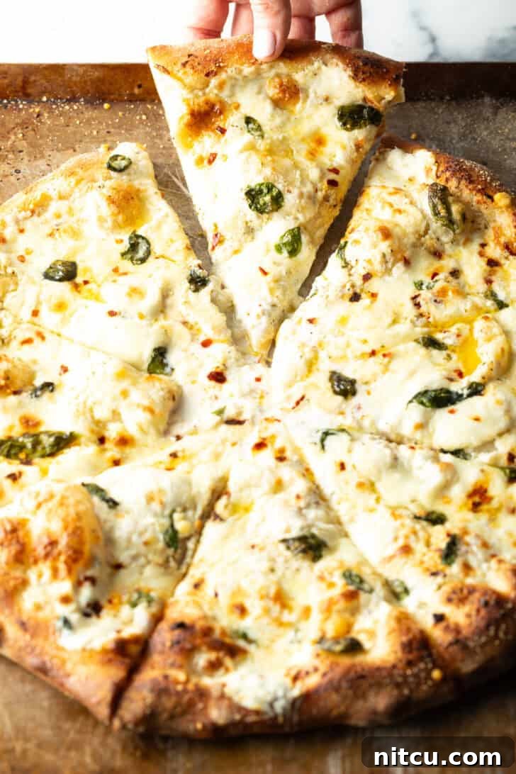 Pizza with white sauce cut into 8 slices. A hand is removing one slice of pizza from the tray.