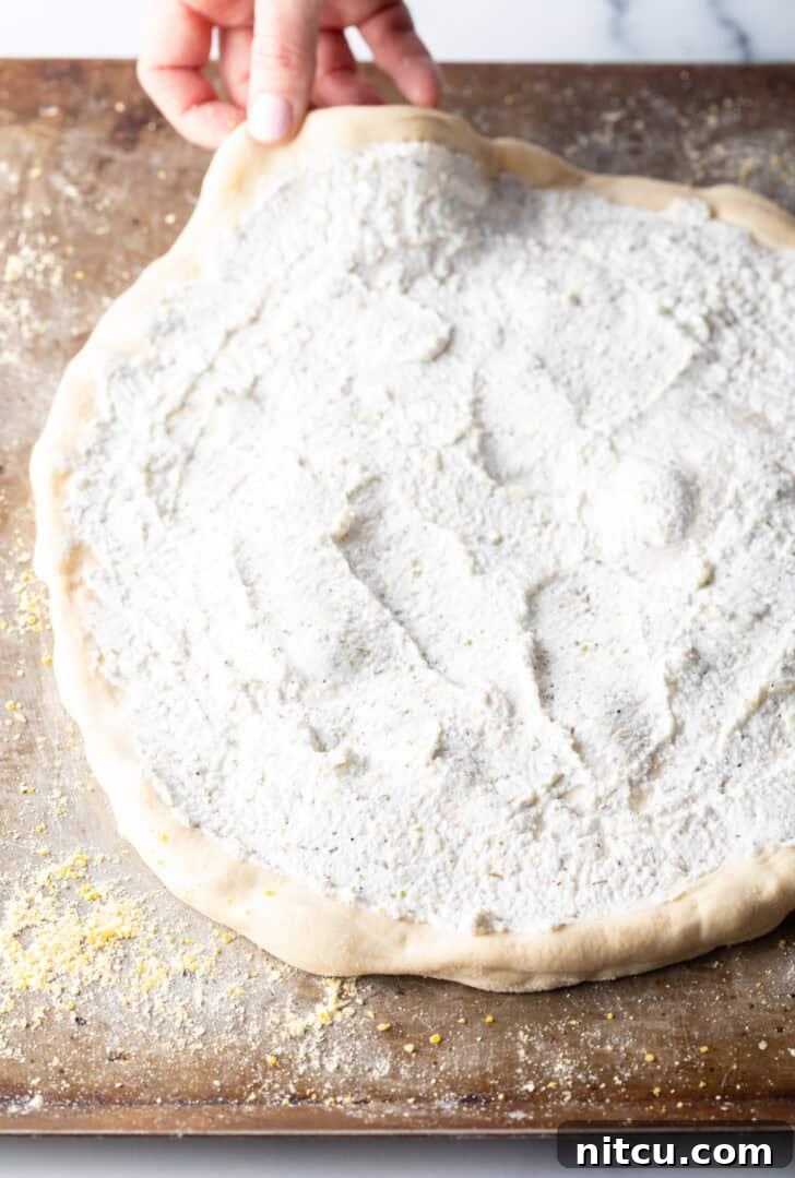 Unbaked pizza crust topped with creamy white sauce.