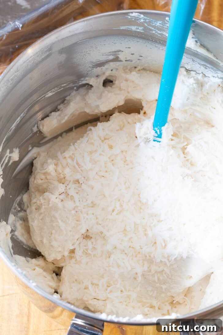 Stirring whipped cream in a metal bowl with a blue spatula.