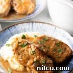 Two boneless pork chops on a plate of mashed potatoes and brown onion gravy, ready to serve.