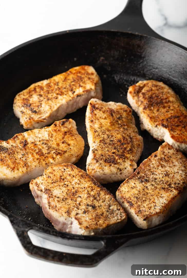 Six boneless pork chops searing to a golden brown in a hot cast iron skillet, developing a delicious crust.