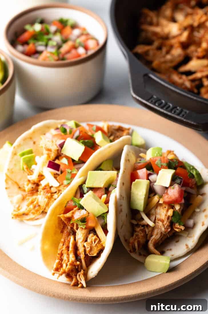 Three chicken tacos with chopped avocado on a plate together, ready to be enjoyed.