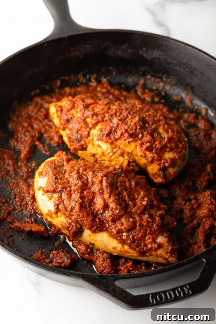 Two chicken breasts simmering in a rich tomato sauce in a cast iron skillet, absorbing the flavors.