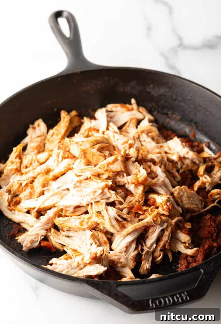 Shredded chicken in a cast iron skillet, perfectly cooked and ready for serving.