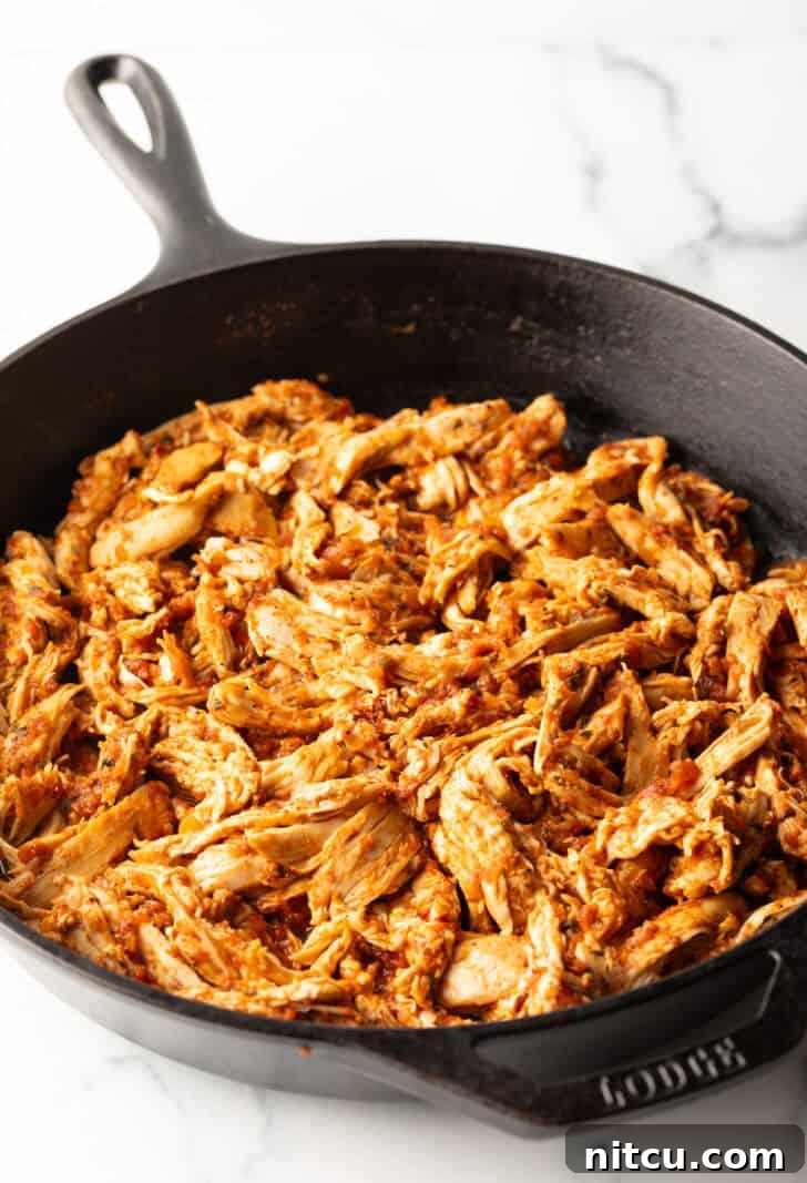 Shredded chicken coated in a luscious tomato sauce in a cast iron skillet, ideal for tacos.