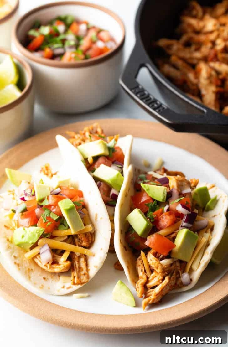 Three chicken tacos with chopped avocado on a plate together, showcasing the finished meal.