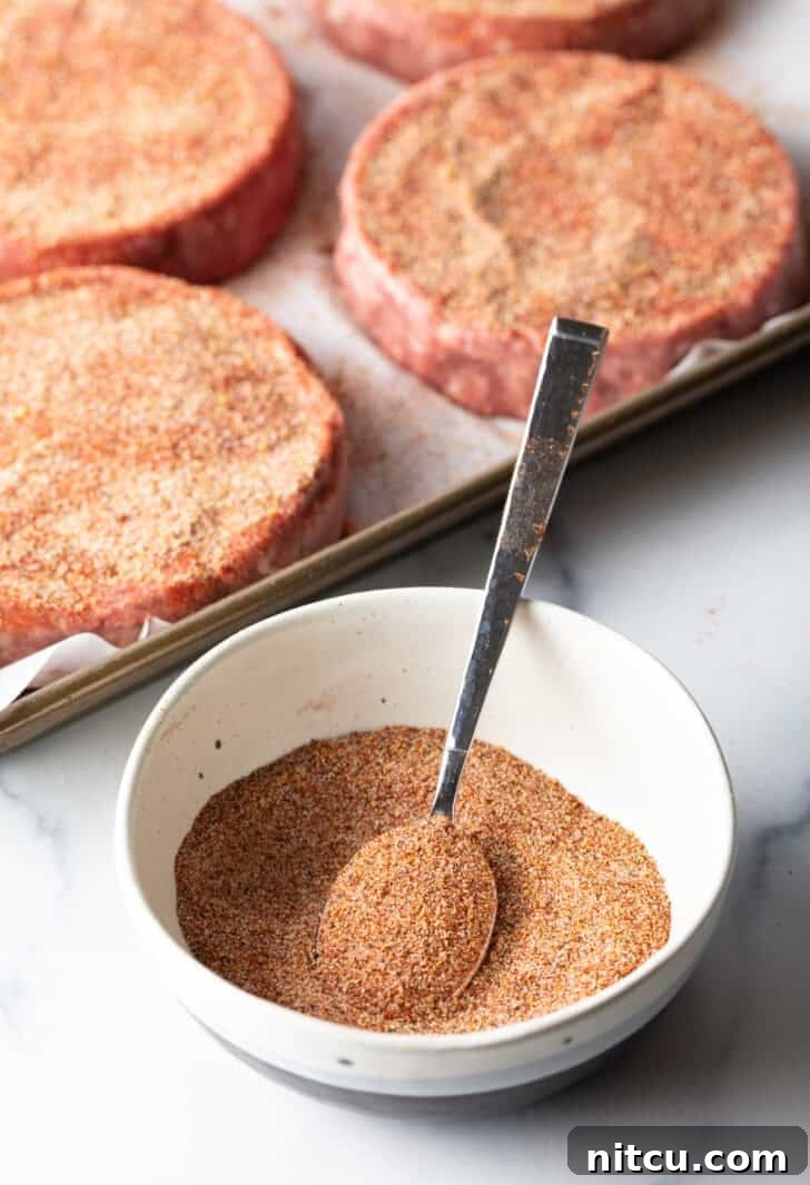 A white bowl brimming with a vibrant blend of homemade burger seasoning, with a spoon resting beside it, ready to infuse flavor.