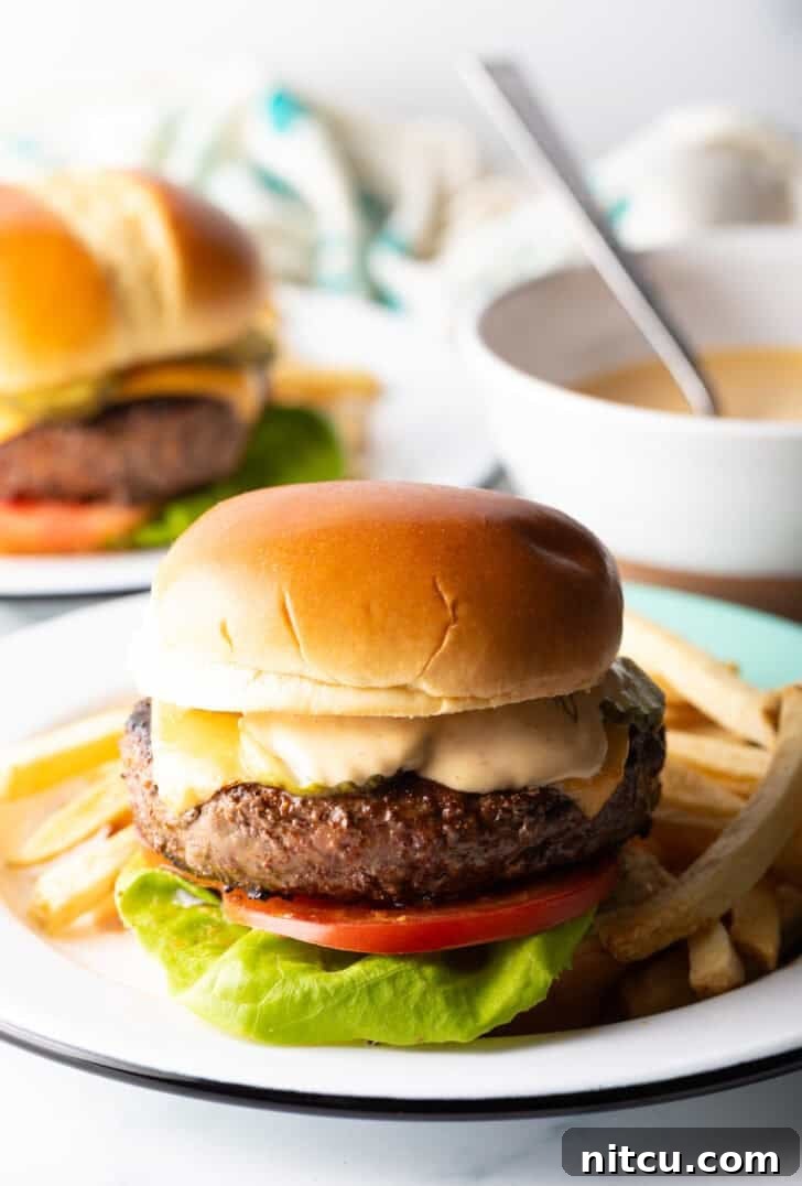 A mouth-watering cheeseburger, perfectly cooked and topped, served alongside a generous portion of golden-brown french fries on a white plate.