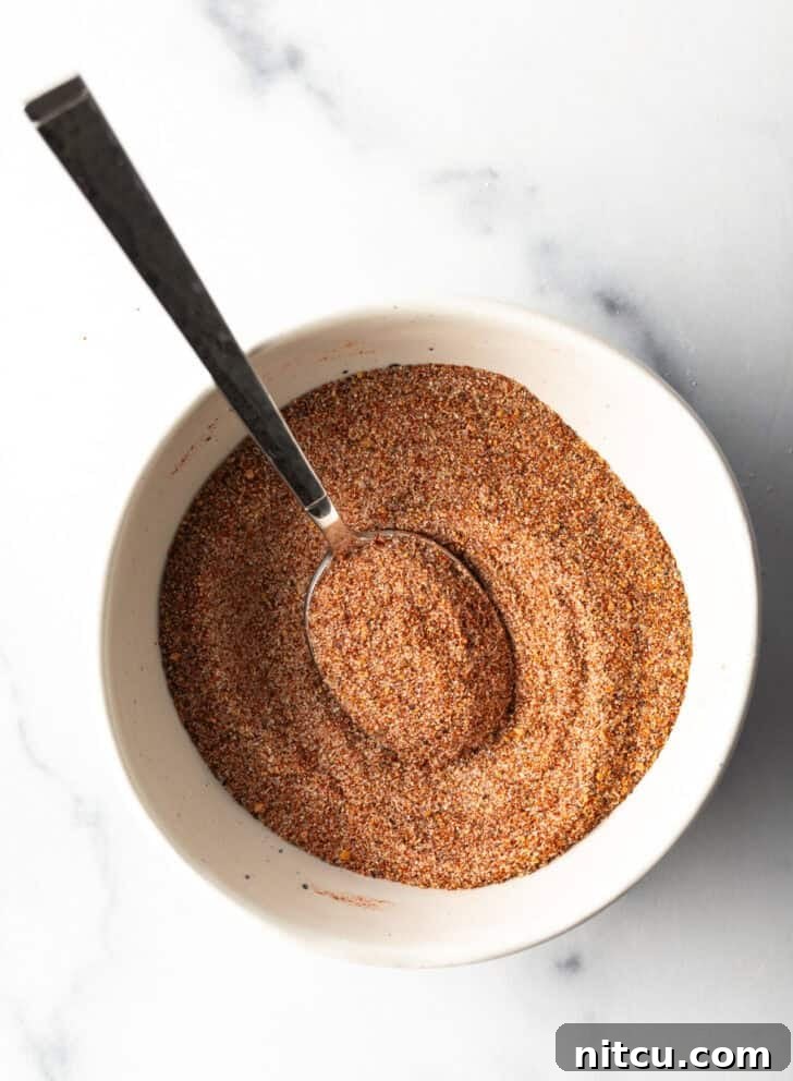 Top-down view of a white bowl filled with the mixed burger seasoning, with a spoon nestled within the spices.