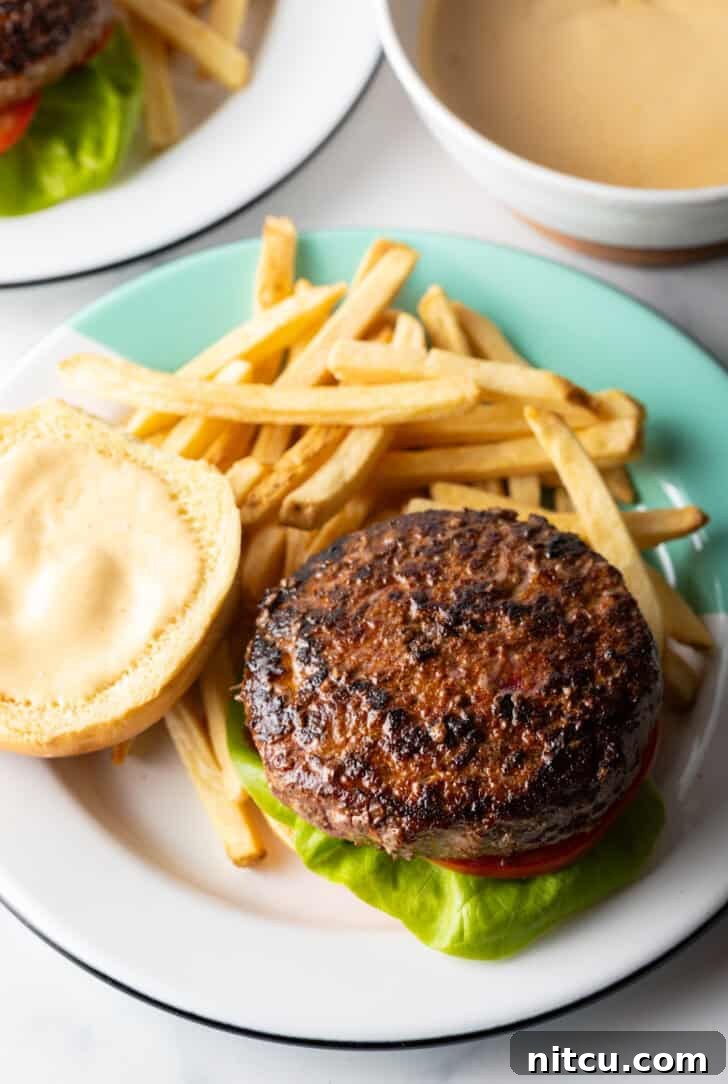 An open-faced burger showcasing its juicy patty and toppings, presented on a plate with crispy french fries.
