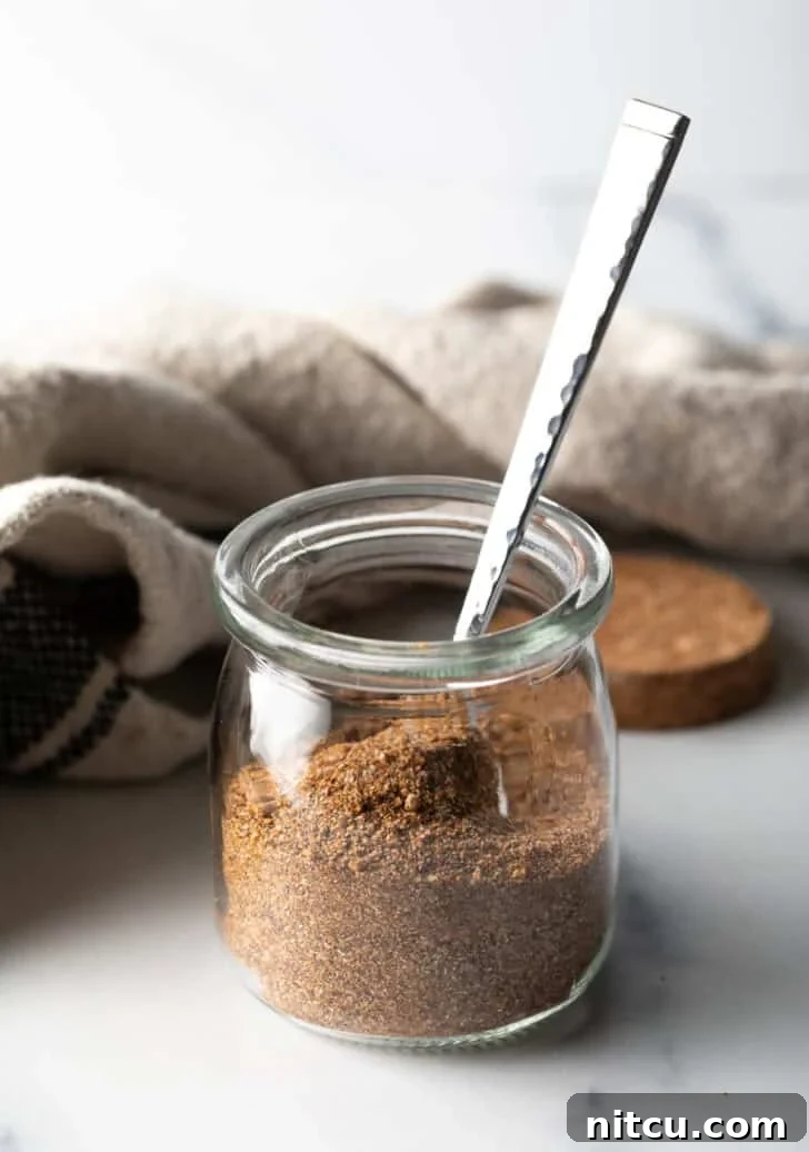 Small glass jar with homemade pork chop seasoning and a metal spoon, ready for use.