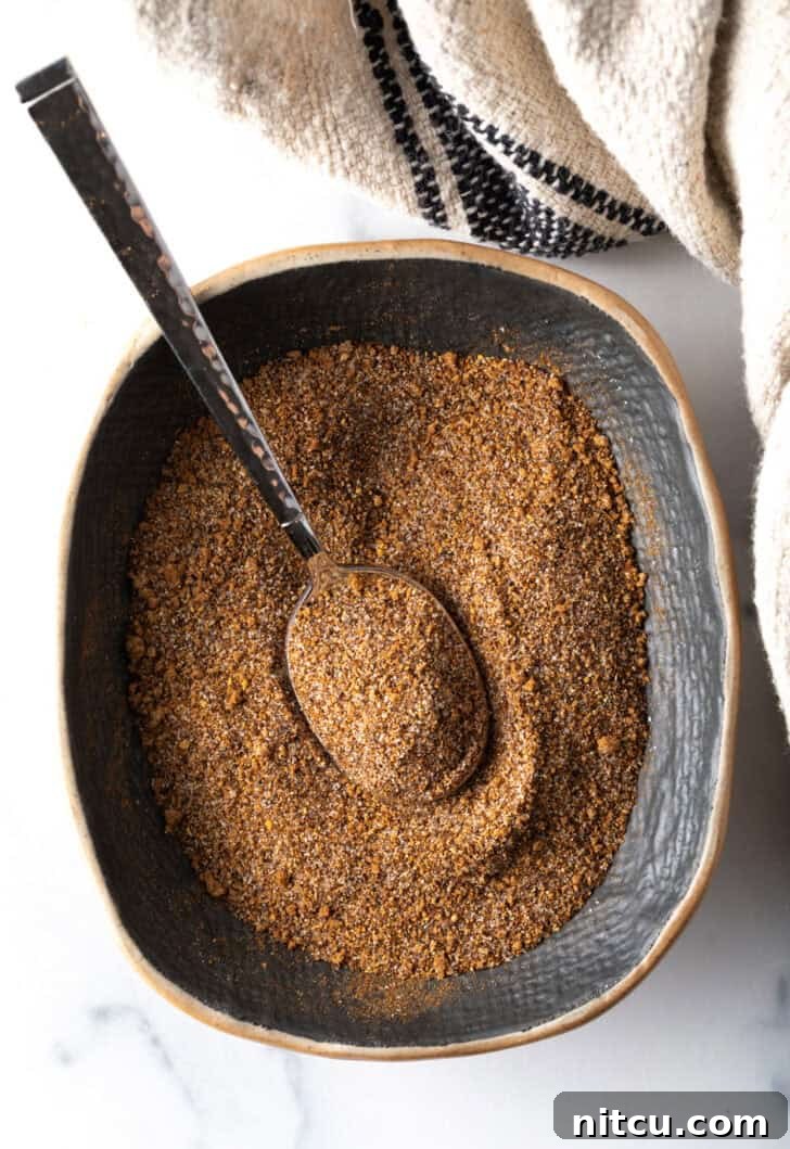 Top down view of a blend of spices in an oval dish with a metal spoon, showcasing the rich colors.