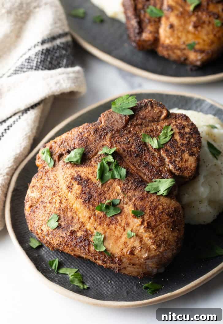 Browned seasoned bone-in pork chop on a plate with mashed potatoes, garnished with chopped parsley, ready to be served.