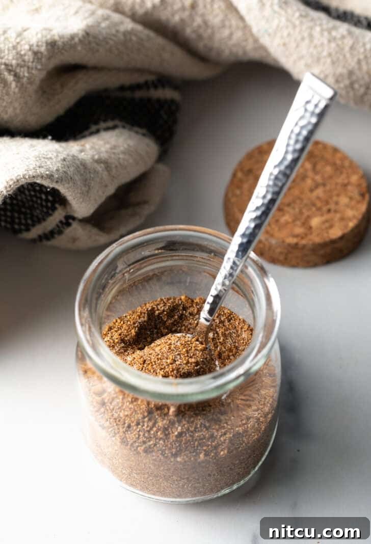 Small glass jar with the finished pork chop seasoning and a metal spoon.
