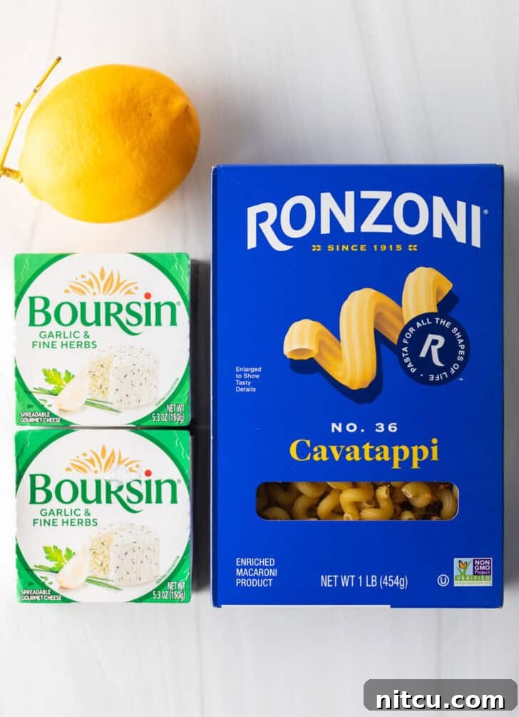 Top-down view of ingredients for Boursin cheese pasta: a box of cavatappi, two boxes of Boursin cheese, and a whole lemon.