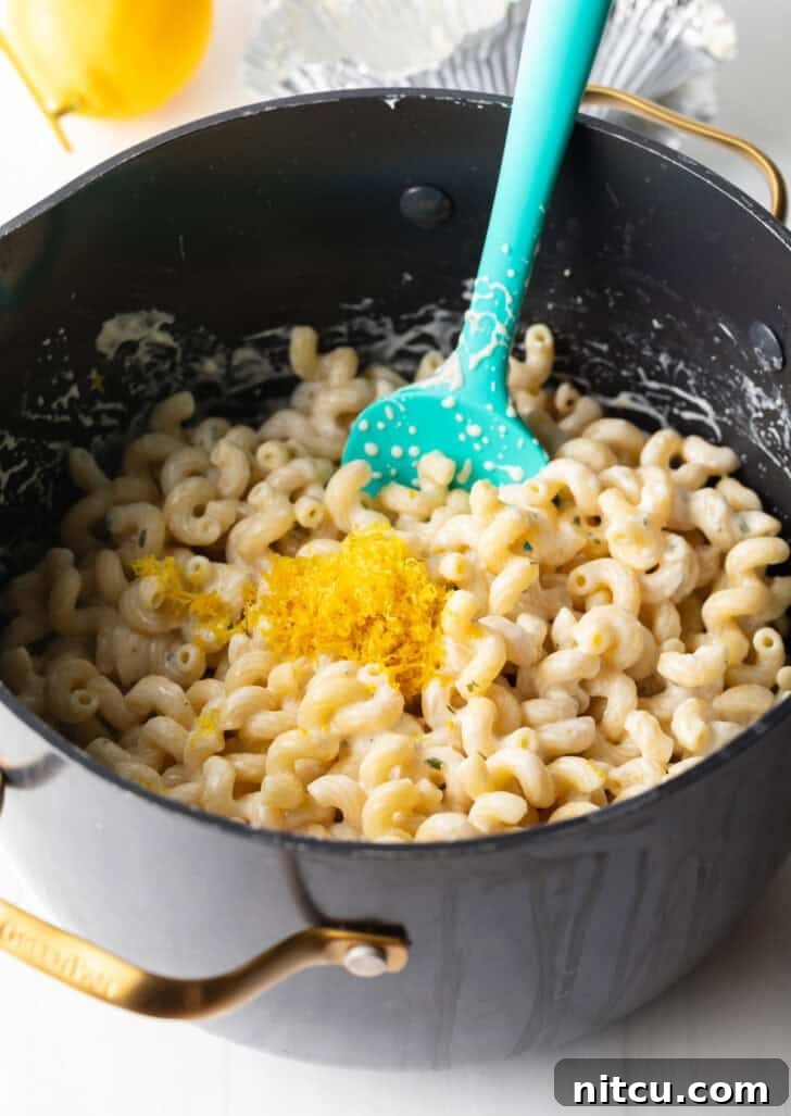 The process of adding Boursin cheese to cooked pasta in a pot.