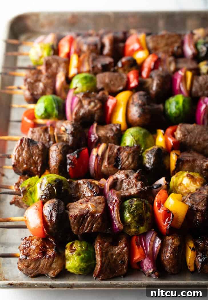 A vibrant display of grilled beef and vegetable kabobs arranged side-by-side, showcasing their delicious char marks and colorful ingredients.