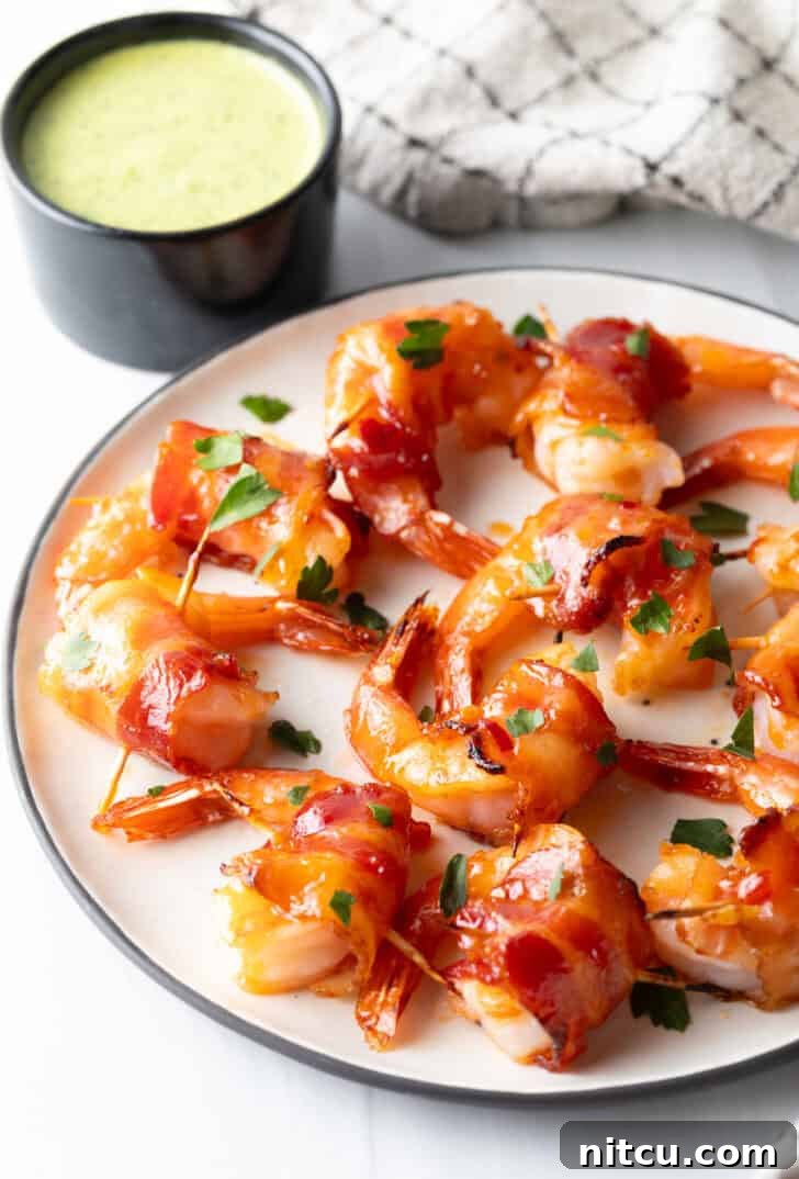 A pristine white plate showcases a delightful arrangement of nearly a dozen golden-brown, bacon-wrapped shrimp, perfectly aligned in a single, enticing layer, highlighting their crispy texture and succulent appearance.