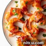 Top down white plate, nearly a dozen bacon wrapped shrimp are loaded onto the plate in a single layer.