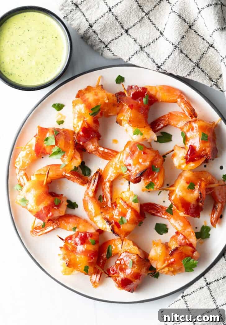 From a top-down perspective, a white plate is beautifully laden with almost a dozen perfectly cooked bacon-wrapped shrimp, arranged neatly in a single, inviting layer, showcasing their golden-brown crispiness and the subtle sheen of the glaze.