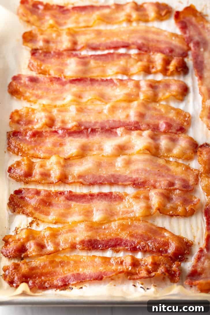 A dozen pieces of bacon are laid out evenly on a baking sheet, partially cooked to a light golden hue, showing just enough crispness to indicate their readiness for the next step of wrapping.