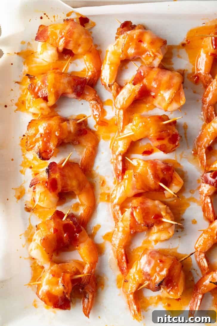 A baking sheet filled with a dozen perfectly cooked bacon-wrapped shrimp, each piece glistening and golden, held together by toothpicks, showcasing their readiness to be served as an enticing appetizer.
