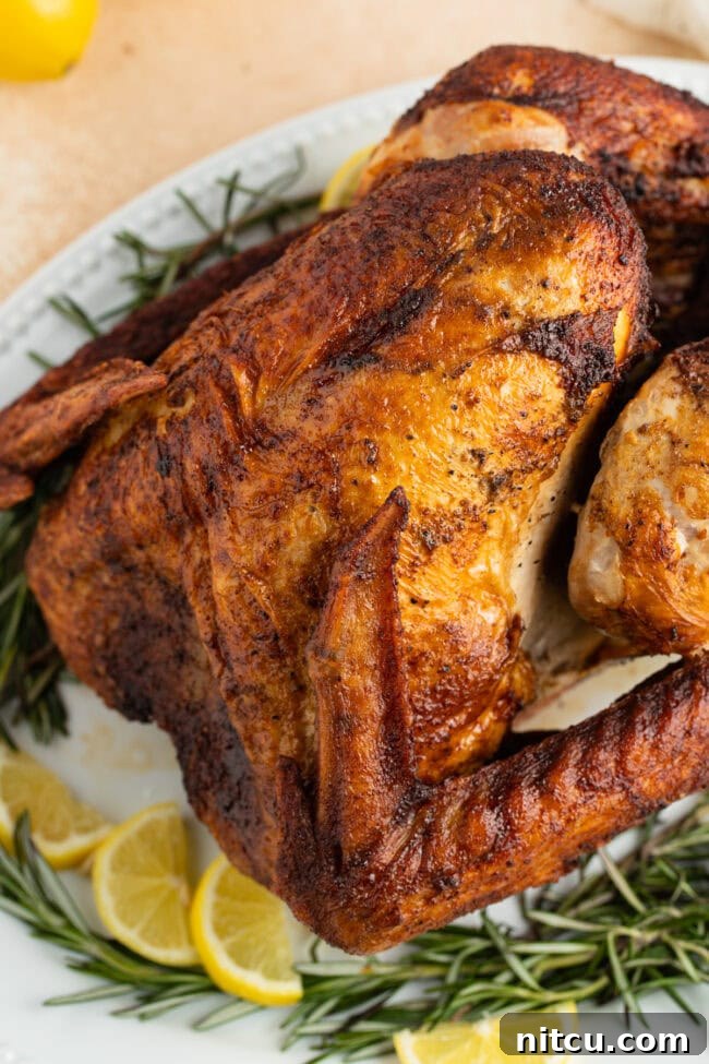 Thanksgiving fried turkey placed on a serving platter with herbs and lemon wedges.
