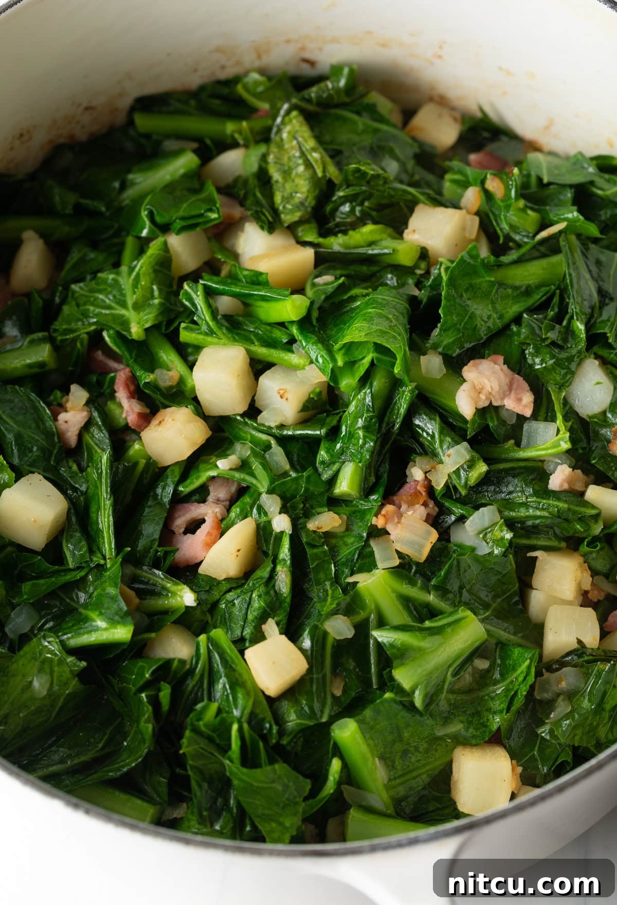 Close-up of collard greens, parsnips, and crispy bacon simmering together in a cast-iron Dutch oven, releasing rich aromas.