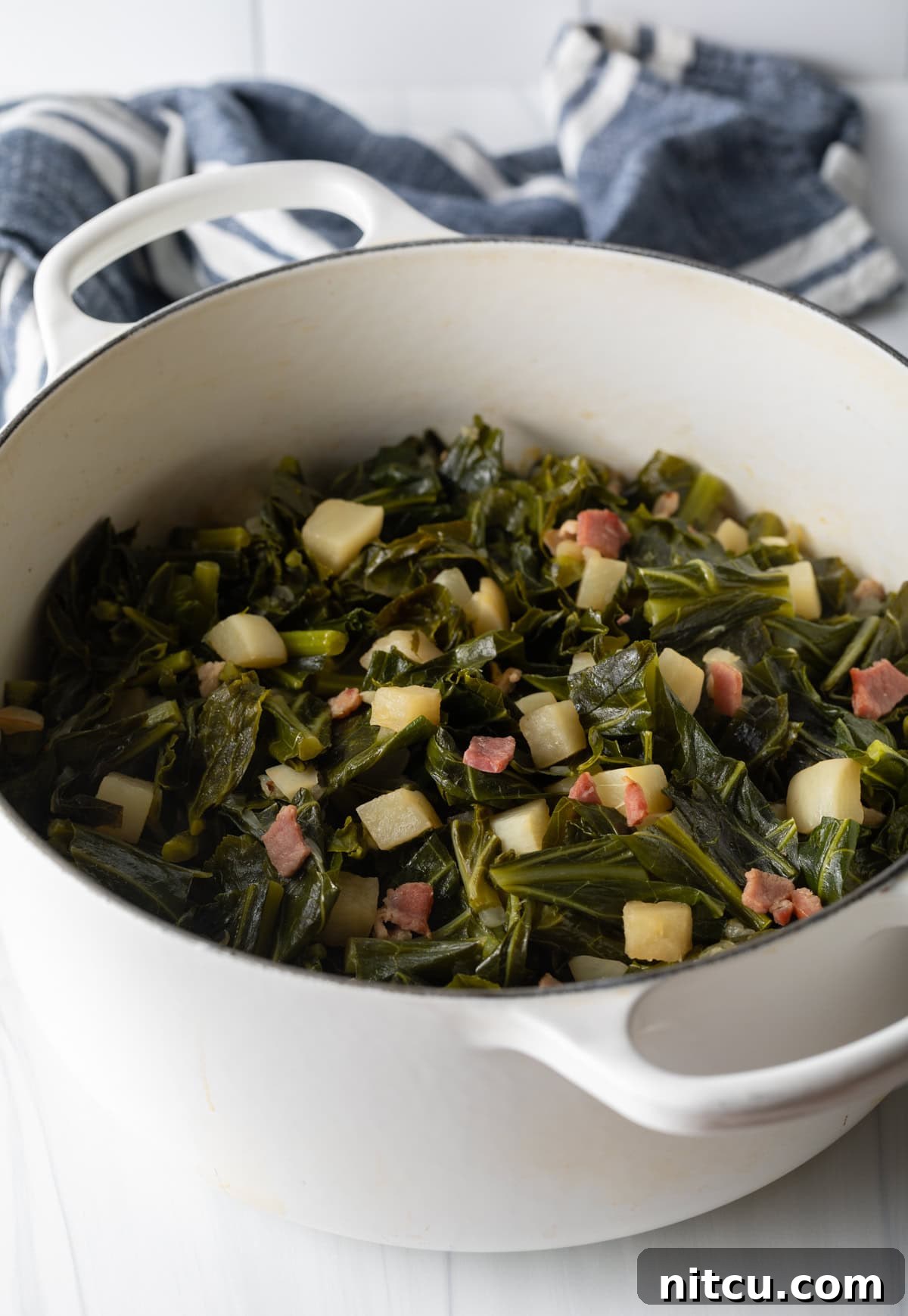 A large Dutch oven filled with glistening, perfectly cooked Southern collard greens, ready to be served hot.