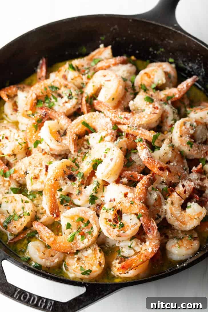 A cast iron skillet filled with perfectly cooked garlic butter shrimp, garnished with fresh herbs and a lemon wedge, ready to be served.
