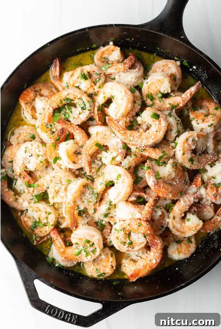 Close-up, top-down view of perfectly cooked shrimp in a black cast iron skillet, generously garnished with fresh parsley.