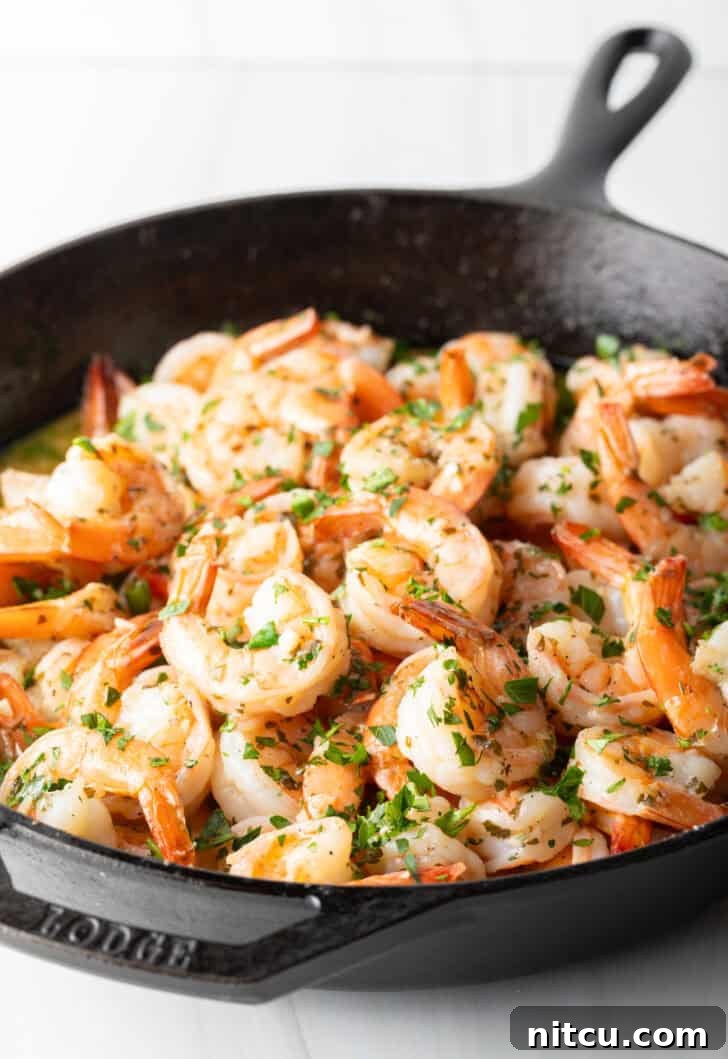 Shrimp in a skillet, turning pink as they cook in the rich garlic butter and white wine sauce, mixed with herbs.