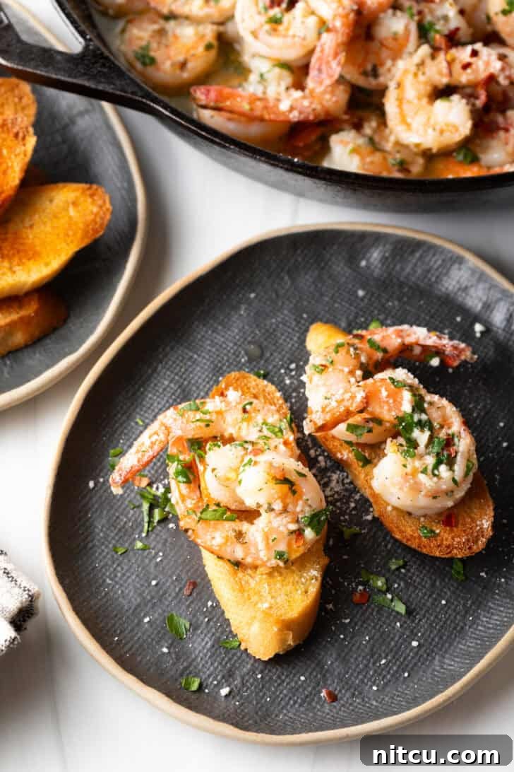 A beautifully plated dish with garlic butter shrimp and baguette slices on a black oval plate, garnished with fresh parsley.
